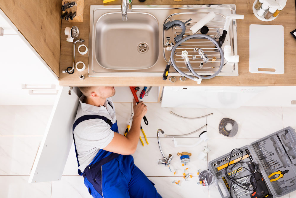 High Angle View Of Male Plumber In Overall Fixing Sink Pipe
